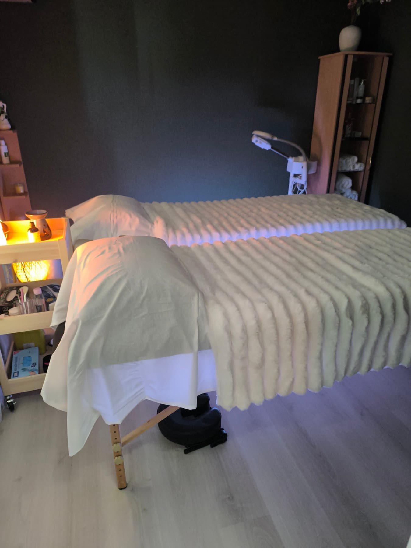 Kaksi hierontapöytää kermanvärisin peittein ja kasvohoitolamppu